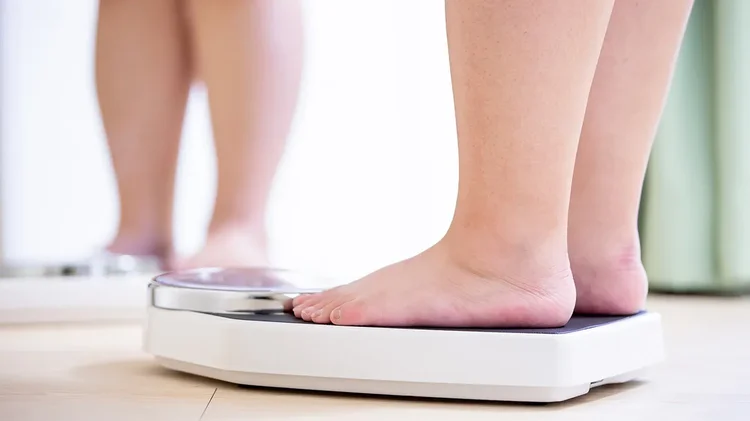 Frau steht barfuß auf einer Waage.