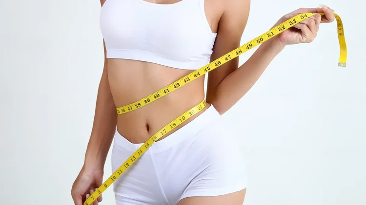 Frau legt gelbes Maßband um Taille.