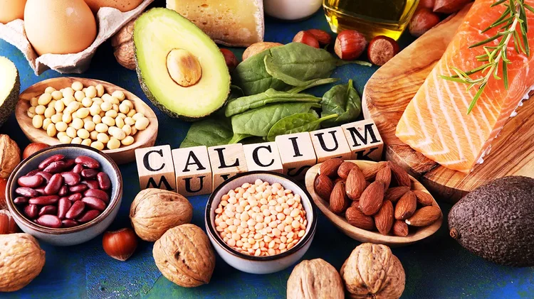 Calciumreiche Lebensmittel wie Avocado, Nüsse, Käse und Lachs auf einem Tisch.