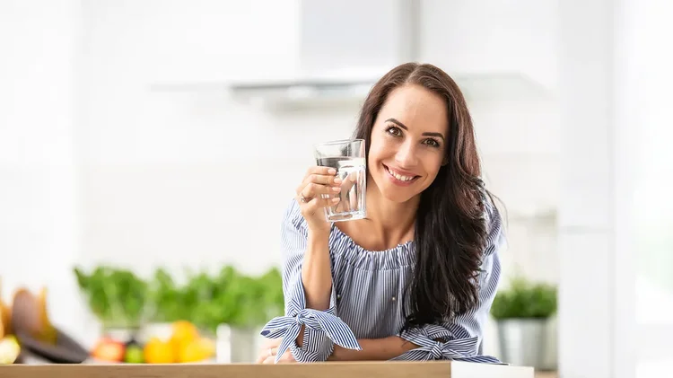 Lächelnde Frau hält Glas Wasser in heller Küche.