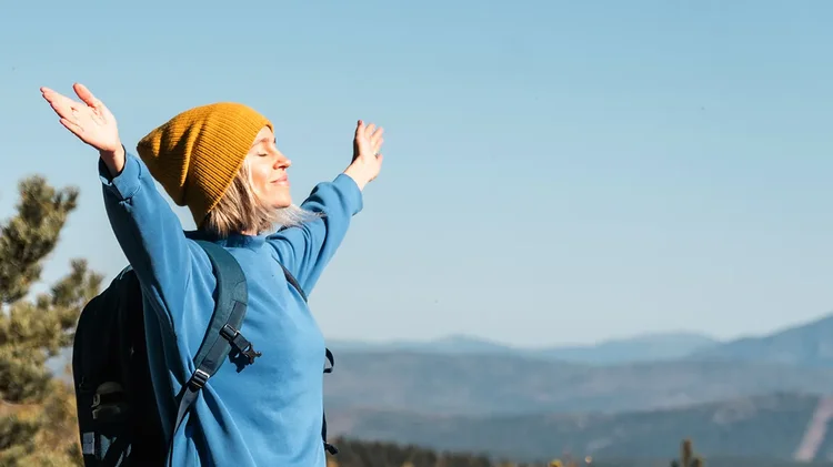 Frau steht mit ausgebreiteten Armen in der Natur und genießt den Moment.