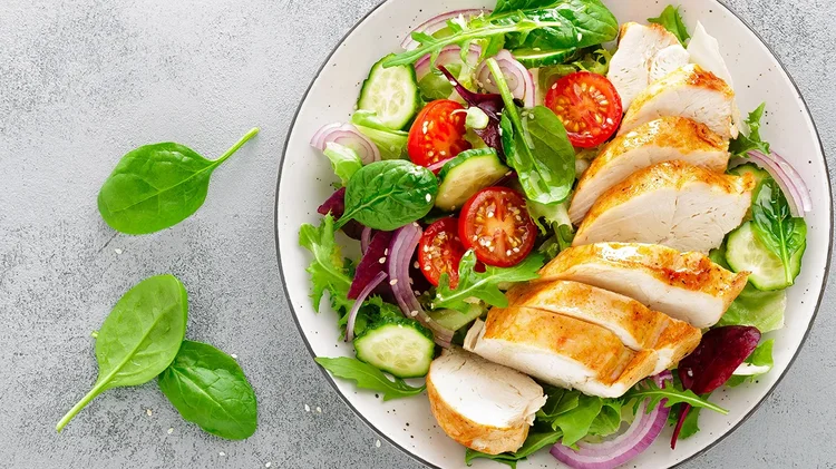 Teller mit Salat aus Gemüse und Hähnchenstreifen.