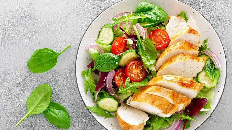 Teller mit Hähnchen und frischem Salat auf grauem Tisch.