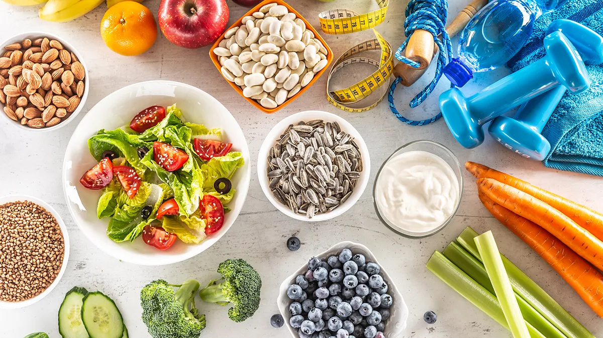 Gesunde Lebensmittel, Hanteln und Maßband auf Tisch als Symbol für ausgewogene Ernährung.