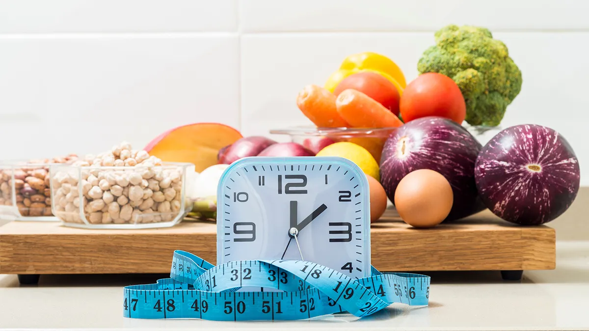 Uhr und frisches Gemüse symbolisieren Intervallfasten und Ernährung.