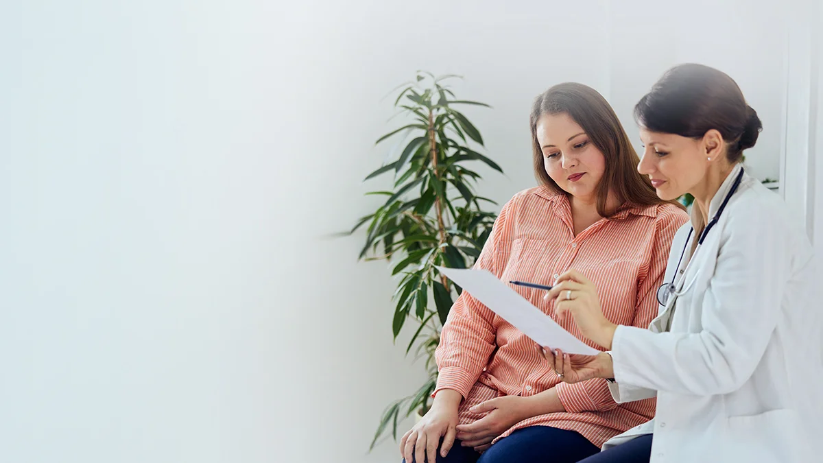 Ärtzin steht neben Patientin mit einem Zettel in der Hand