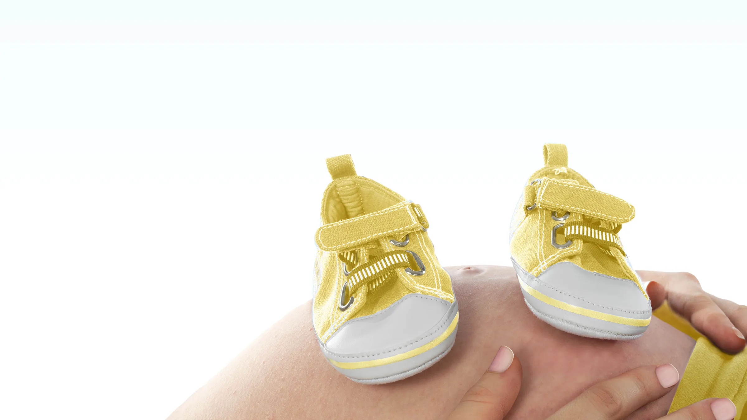 Gelbe Babyschuhe stehen auf einem schwangeren Bauch.
