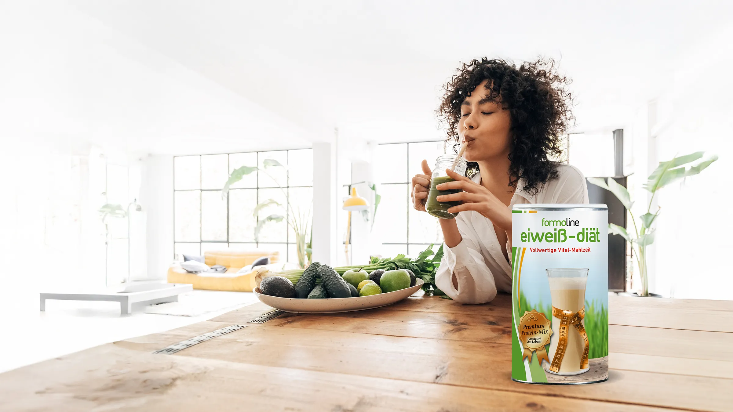 Frau trinkt Smoothie, Dose formoline eiweiß-diät steht auf Tisch mit Avocados und Äpfeln.