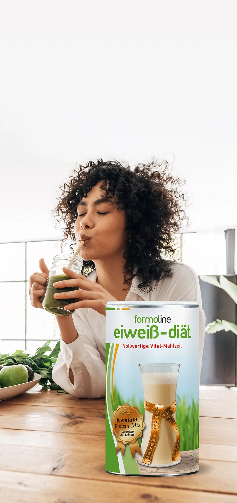 Frau trinkt Smoothie, Dose formoline eiweiß-diät steht auf Tisch mit Avocados und Äpfeln.