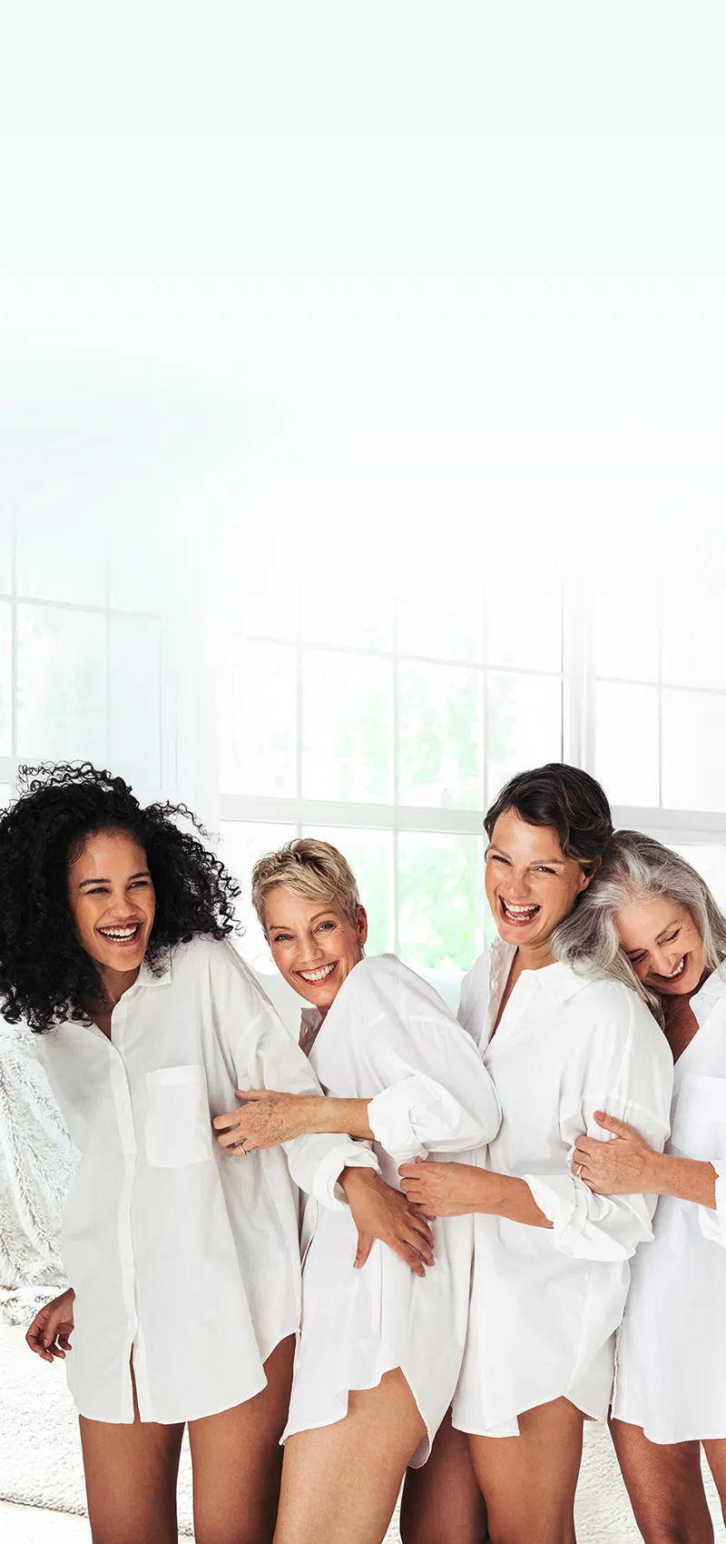 Vier Frauen in weißer Kleidung lachen zusammen in heller Umgebung.