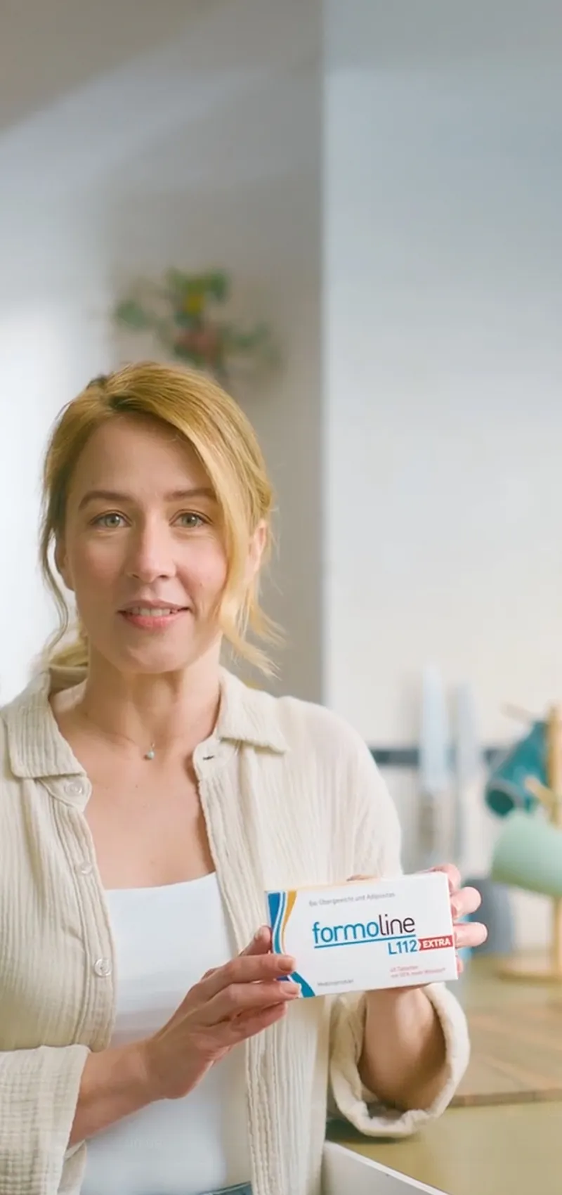 Frau hält formoline L112 EXTRA Packung in heller Küche, Szene aus TV-Spot.