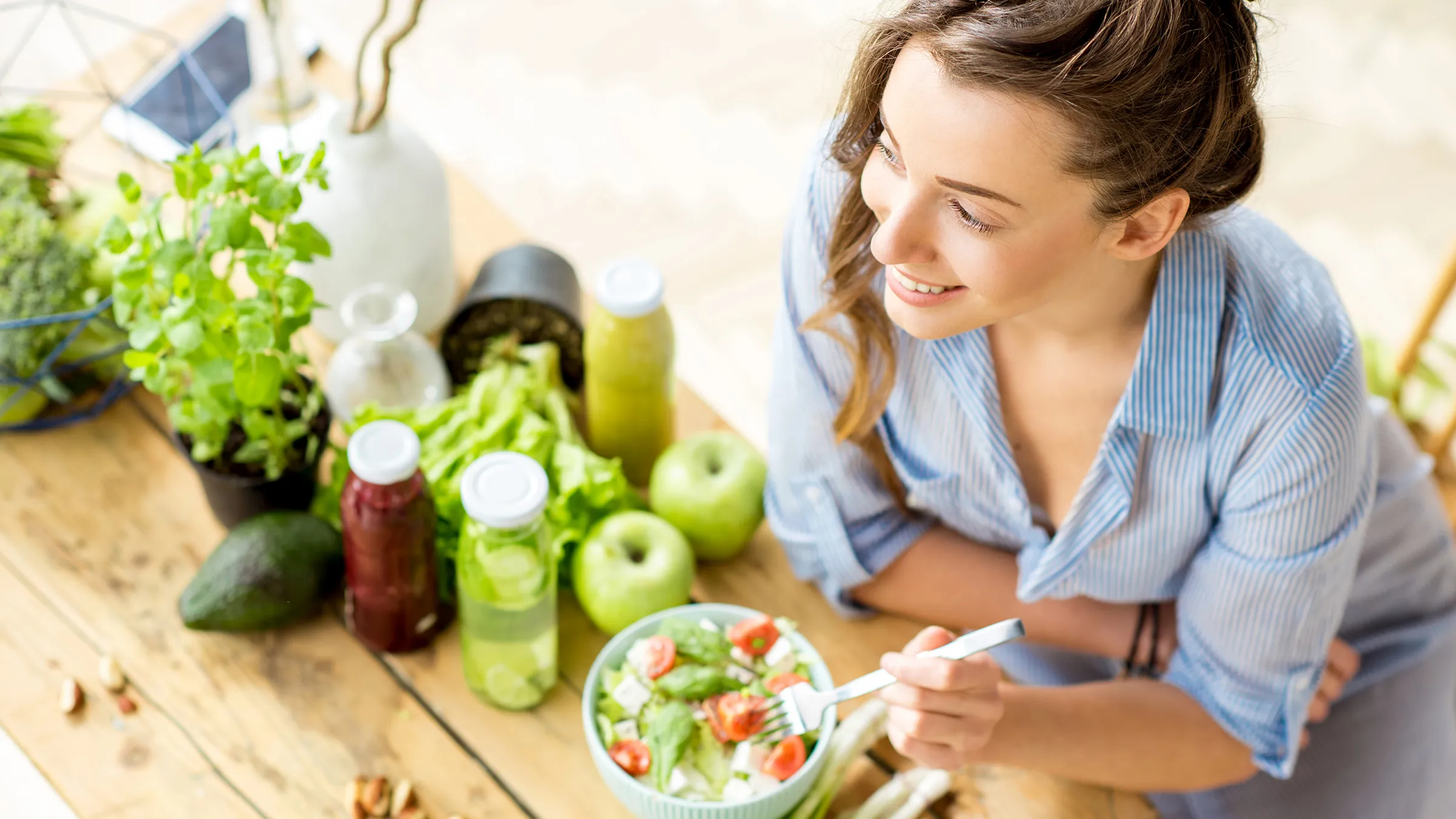 Frau isst gesunden Salat und umgeben von frischen Lebensmitteln.