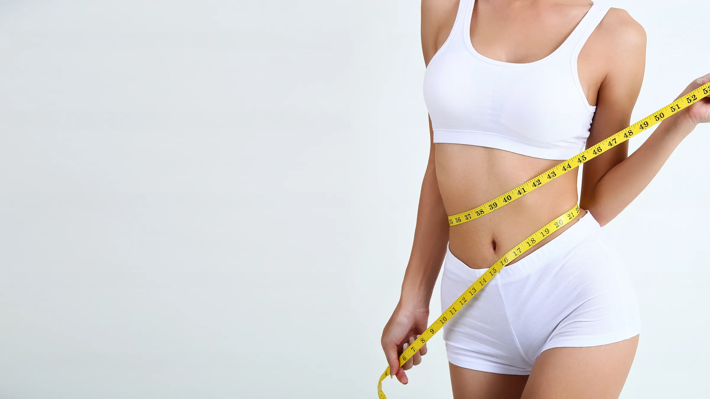 Frau misst mit einem Maßband ihre Taille im weißen Sportoutfit.