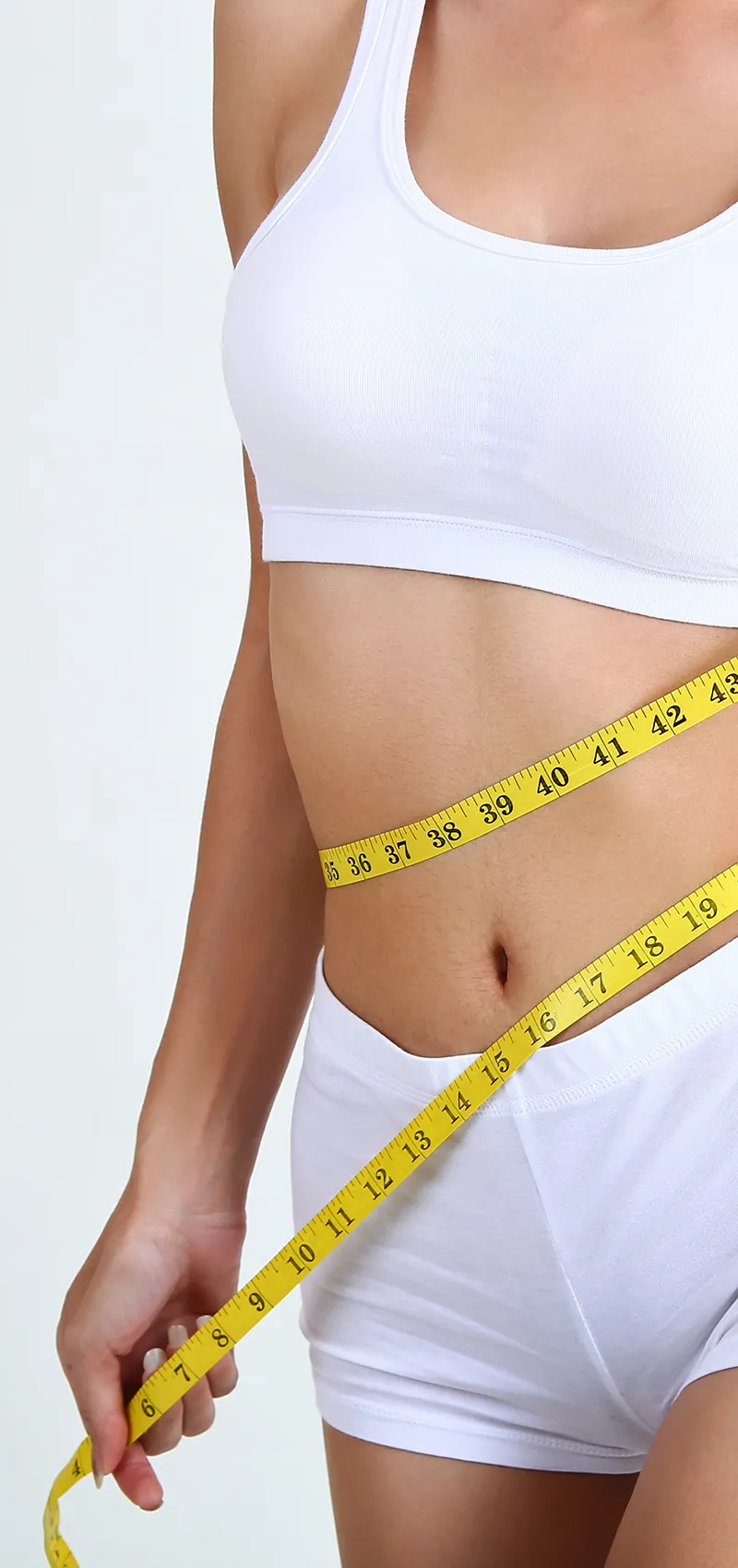 Frau misst mit einem Maßband ihre Taille im weißen Sportoutfit.