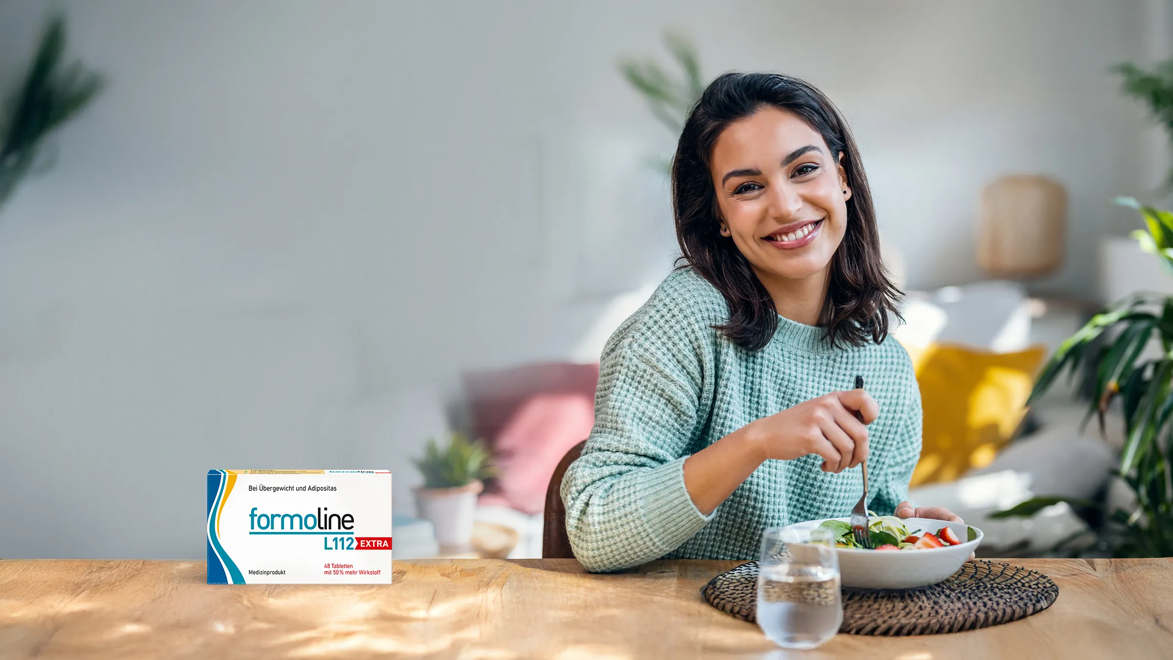Frau isst gesunden Salat mit formoline L112 EXTRA Packung auf dem Tisch.