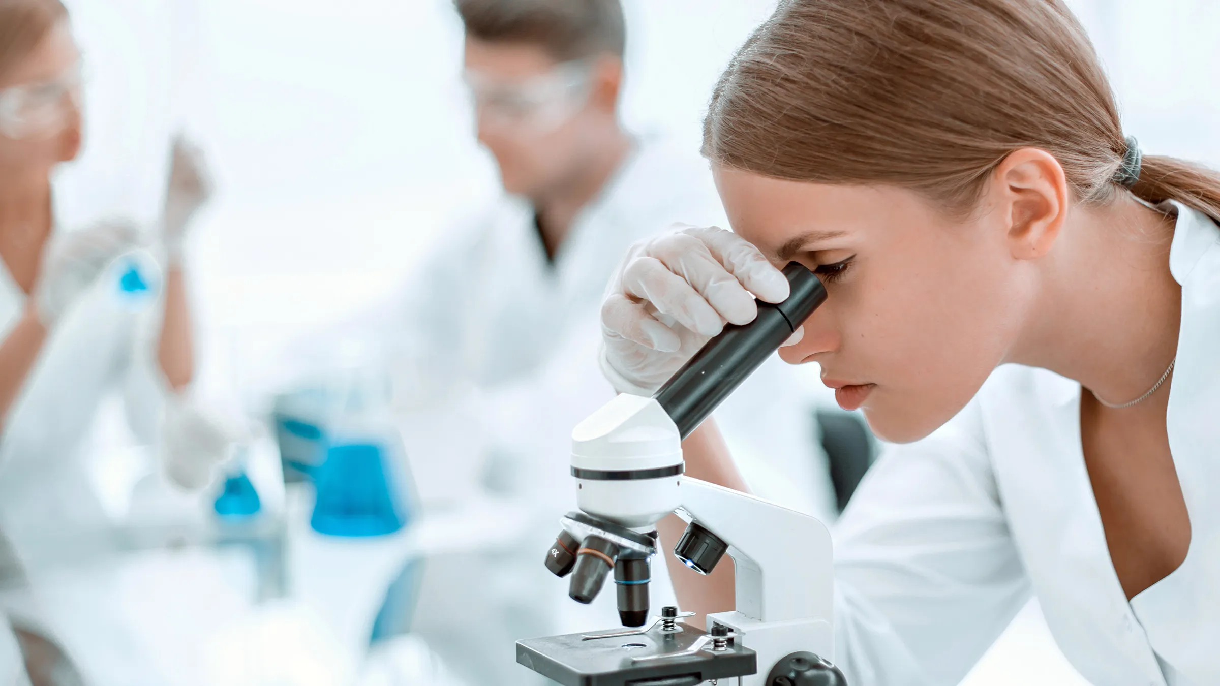 Wissenschaftlerin schaut durch Mikroskop im Labor.