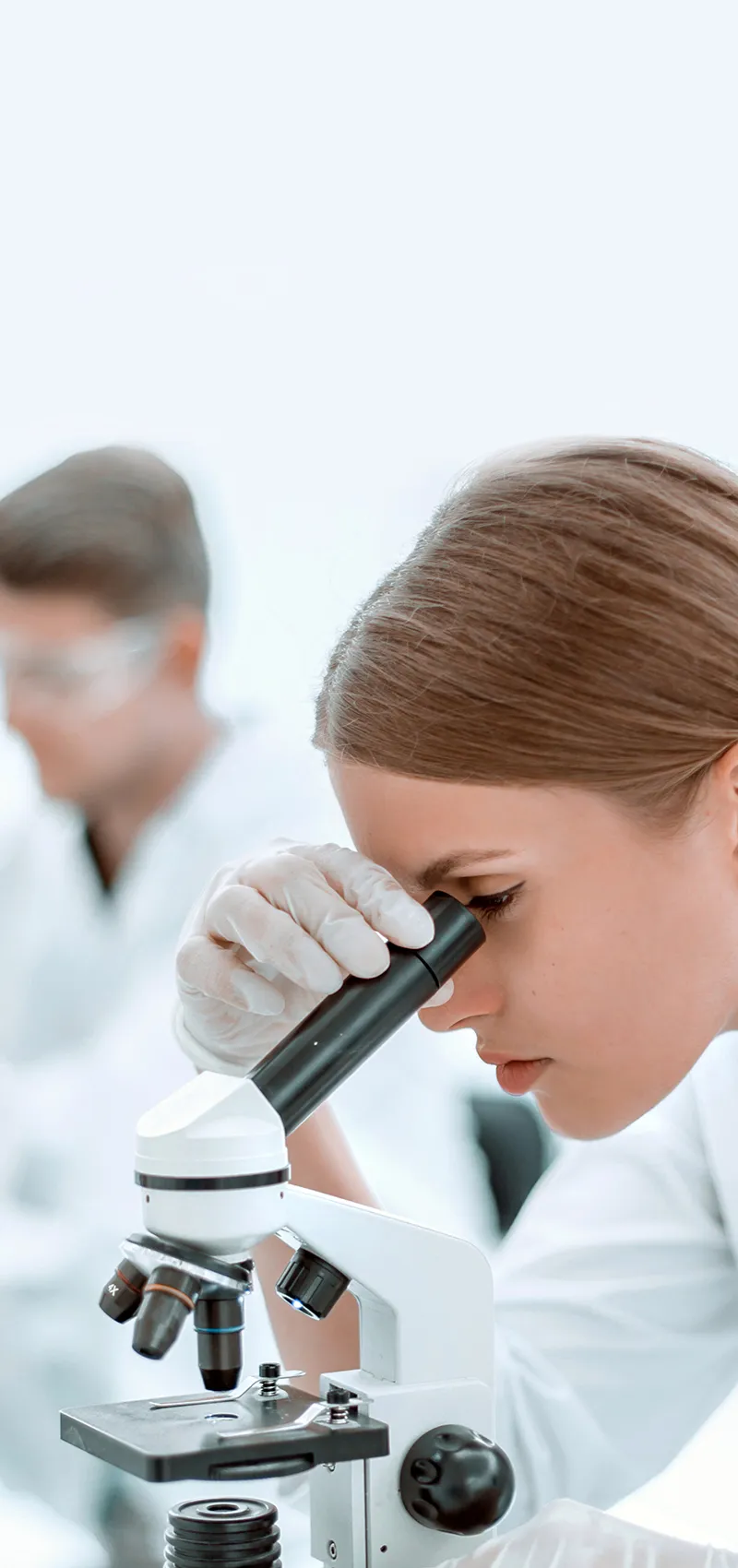 Wissenschaftlerin schaut durch Mikroskop im Labor.