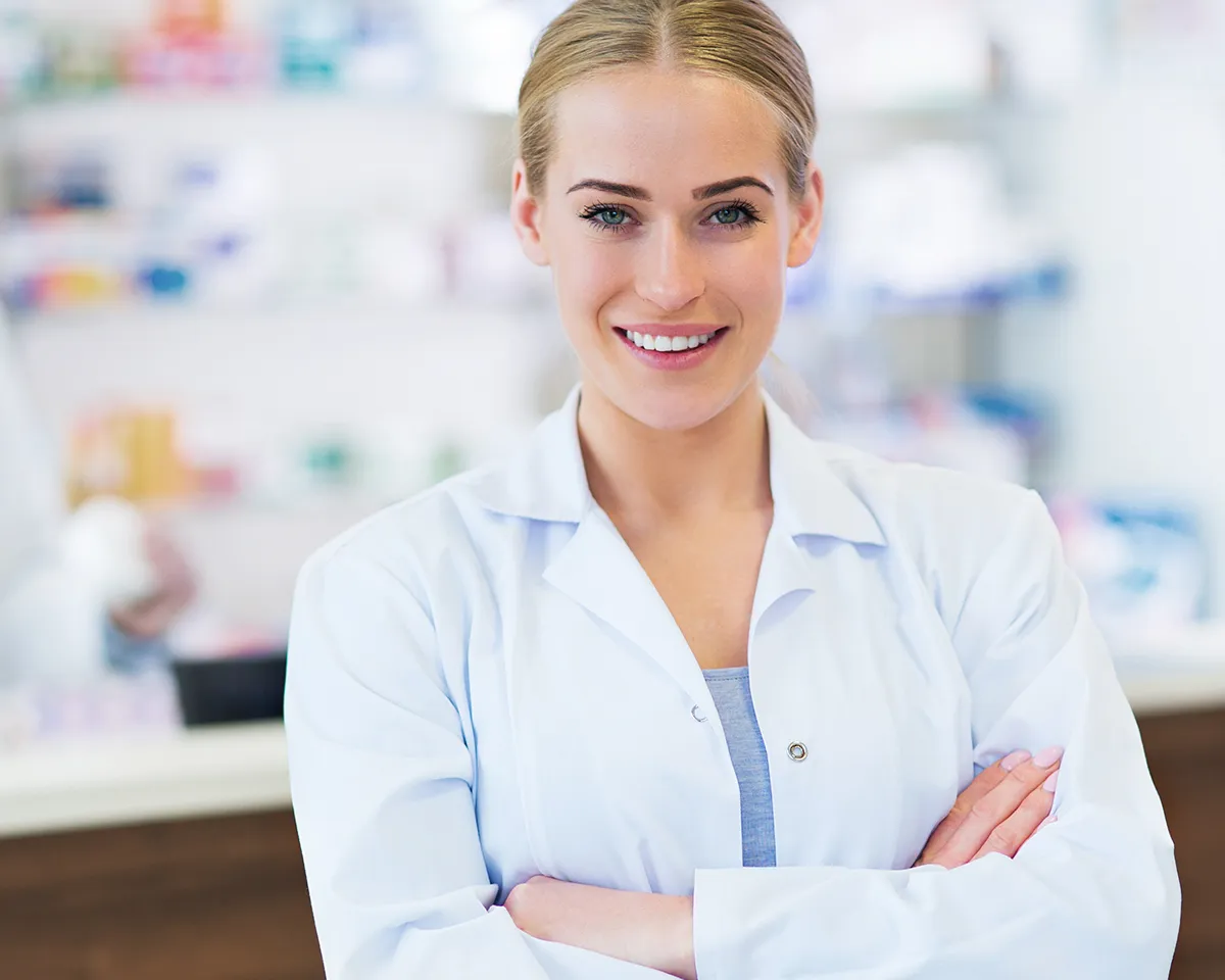 Lächelnde Apothekerin mit weißem Kittel in Apotheke.