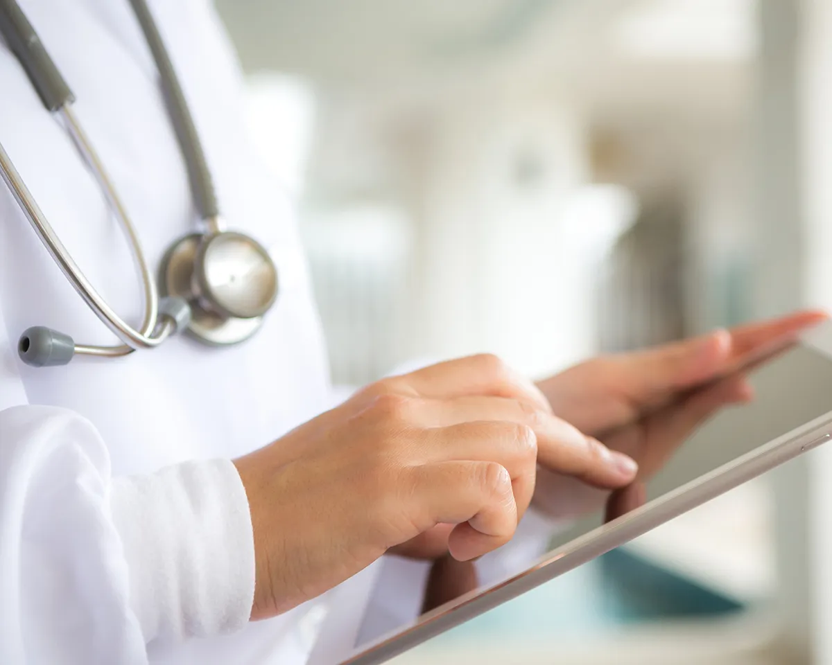 Arzt oder Ärztin mit Stethoskop nutzt Tablet.