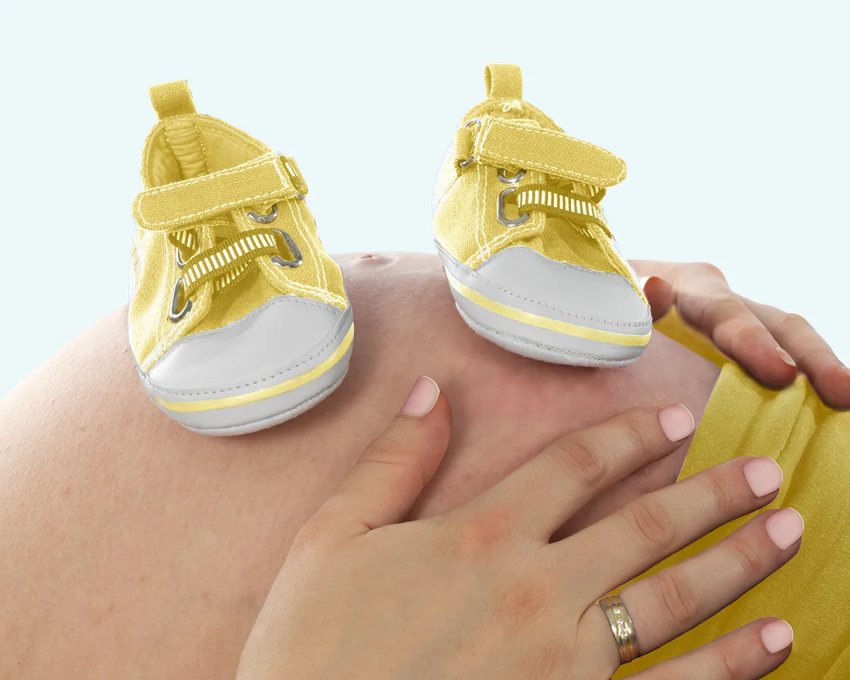 Schwangerschaftsbauch mit gelben Babyschuhen.