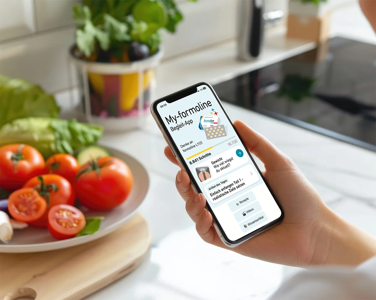 Smartphone mit geöffneter Formoline-App und Gemüse im Hintergrund.