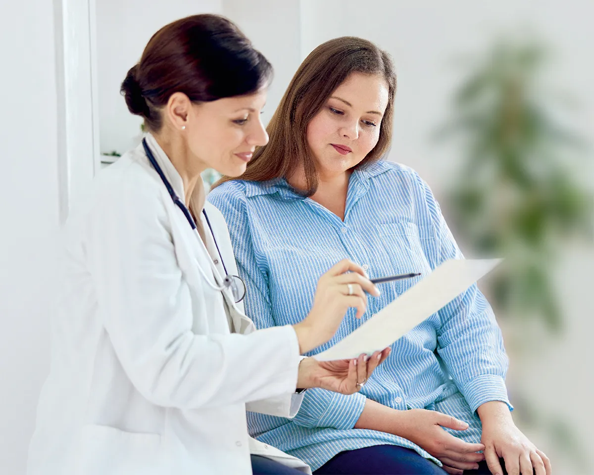 Ärztin zeigt Patientin Untersuchungsergebnisse auf Papier.