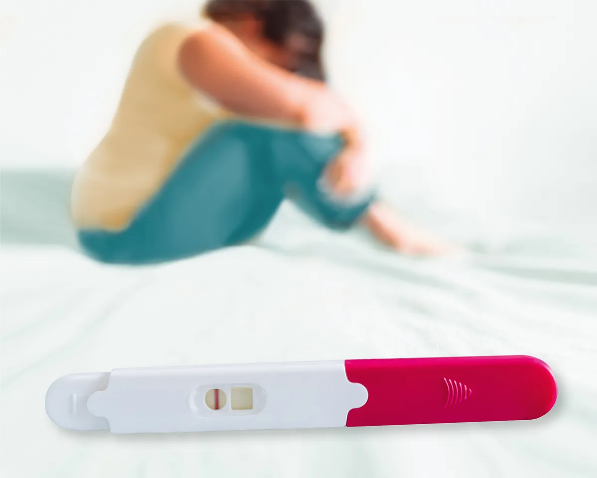 Schwangerschaftstest im Vordergrund, traurige Frau im Hintergrund.