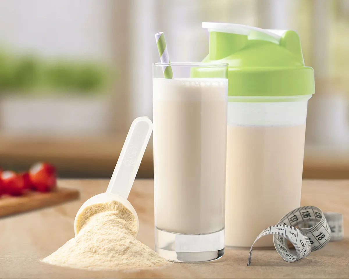 Proteinshake, Pulver und Maßband auf Tisch.