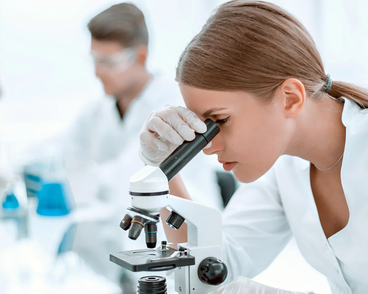 Frau im Labor schaut durch Mikroskop.