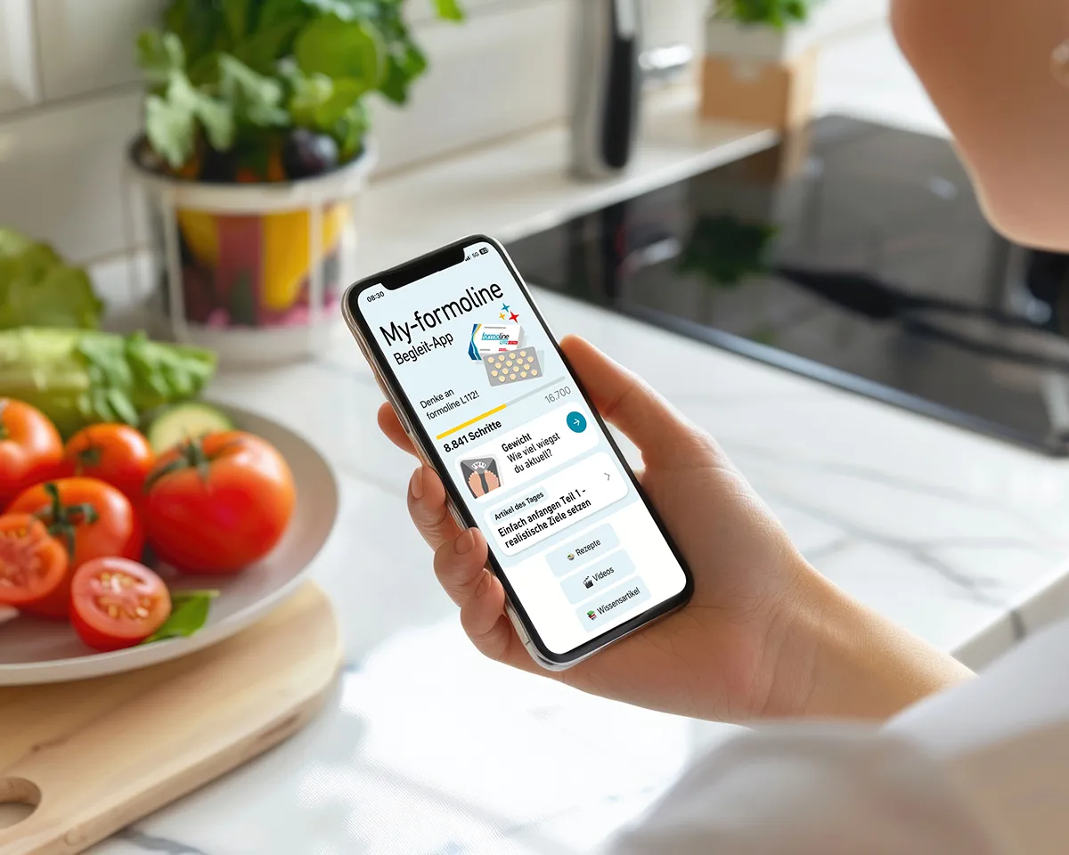 Mensch benutzt formoline App auf dem Smartphone über Arbeitsfläche mit Gemüse