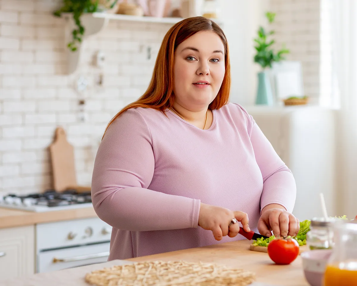 Frau in rosafarbenem Oberteil schneidet Gemüse in heller Küche.