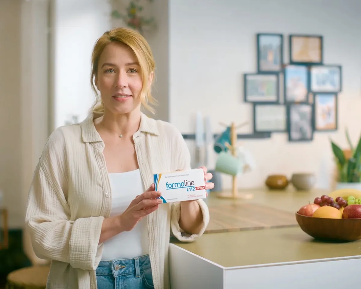 Frau hält formoline L112 EXTRA Packung in heller Küche.