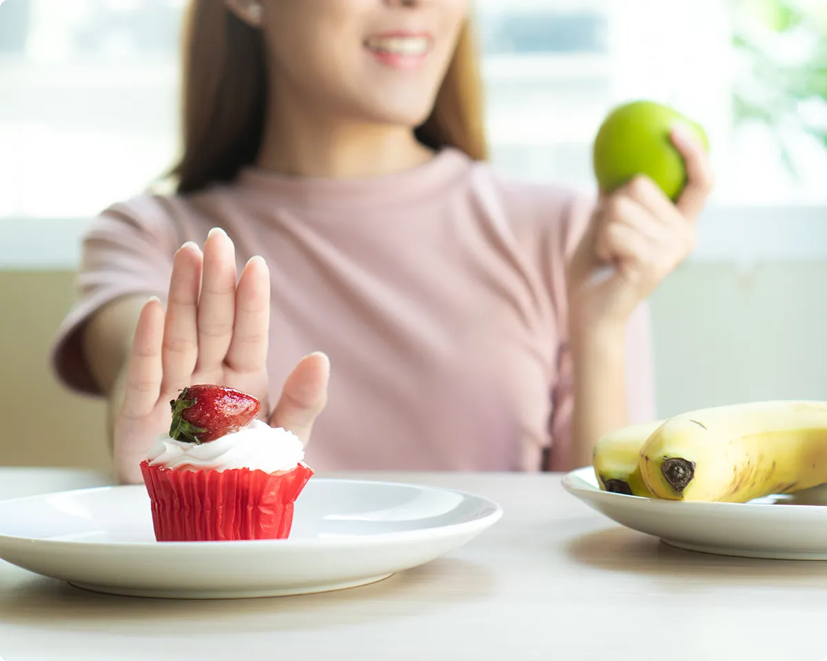 Frau lehnt Muffin ab und hält einen Apfel in der Hand.