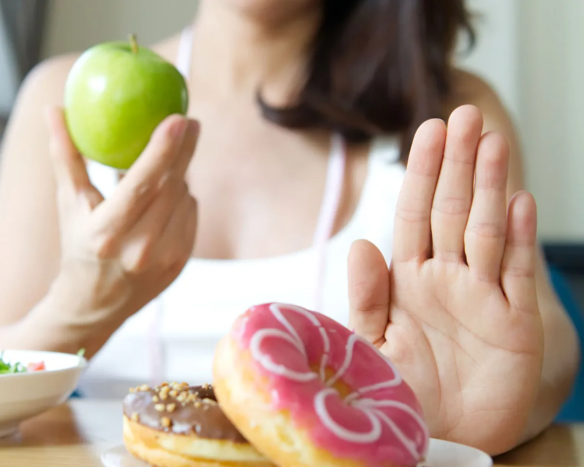 Frau hält Apfel und lehnt Donut mit der Hand ab.