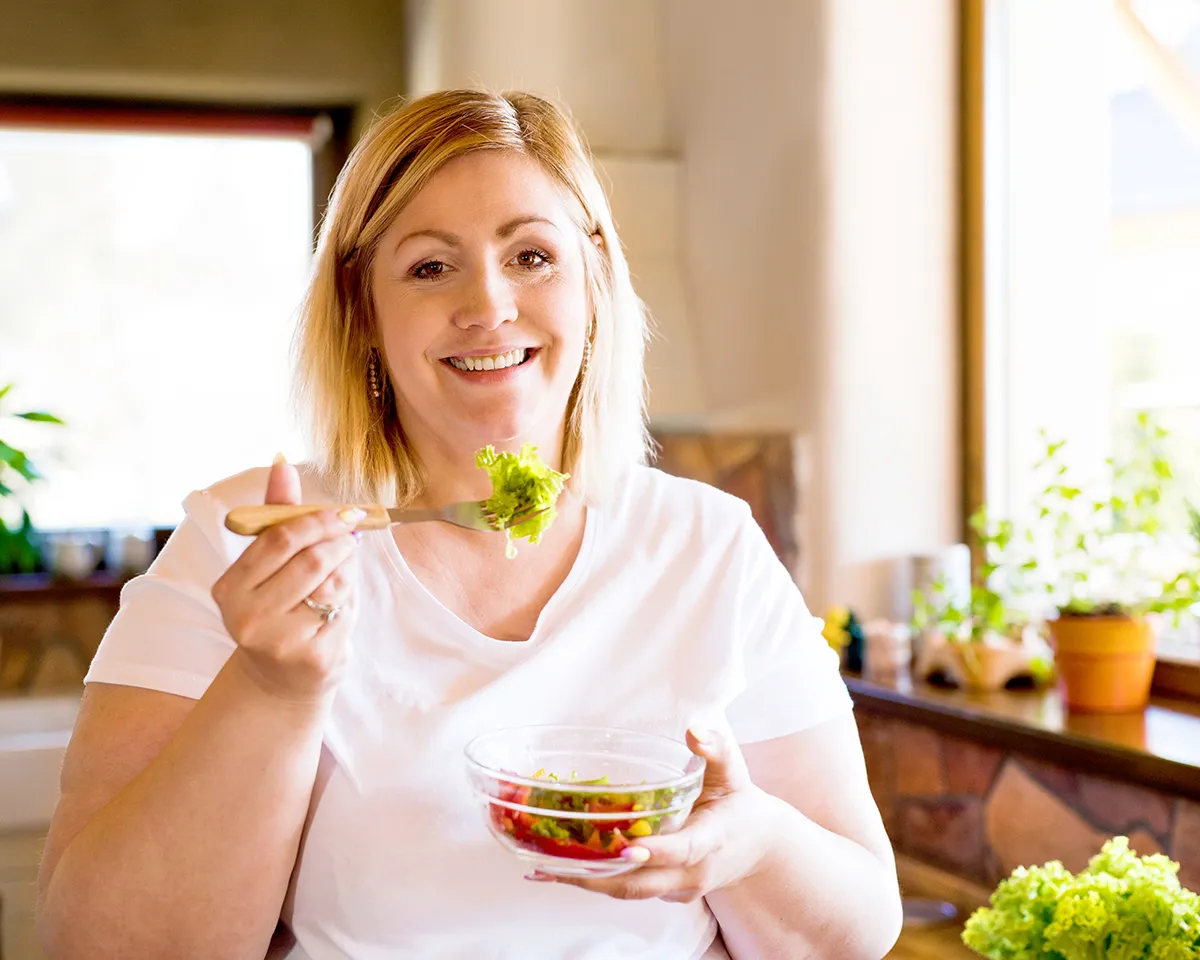 Lächelnde Frau isst frischen Salat in heller Küche.