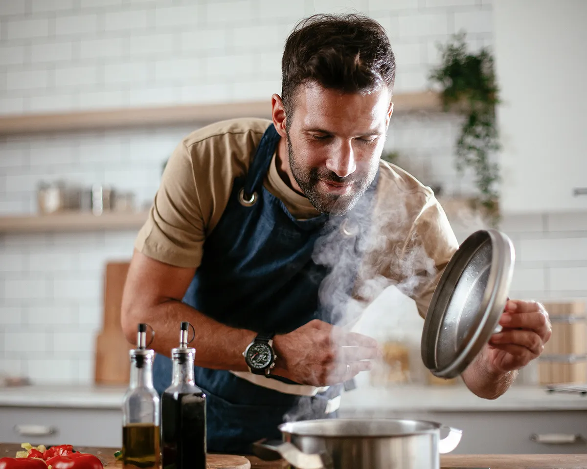 Mann hebt Topfdeckel und kocht in moderner Küche.