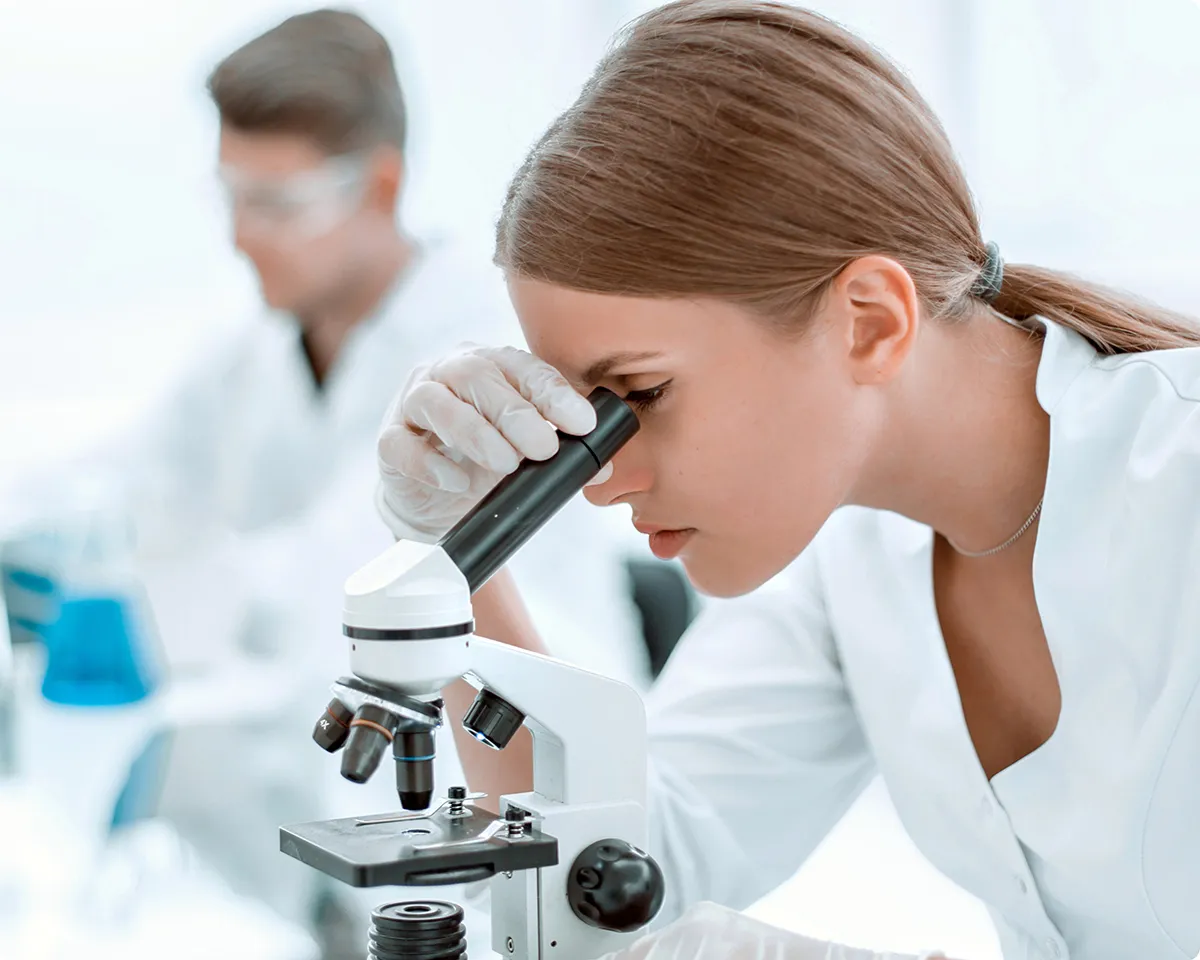 Wissenschaftlerin schaut durch Mikroskop im Labor.