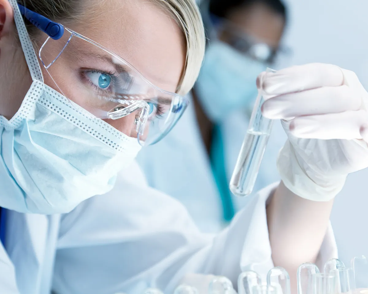 Wissenschaftlerin mit Schutzbrille betrachtet Reagenzglas im Labor.